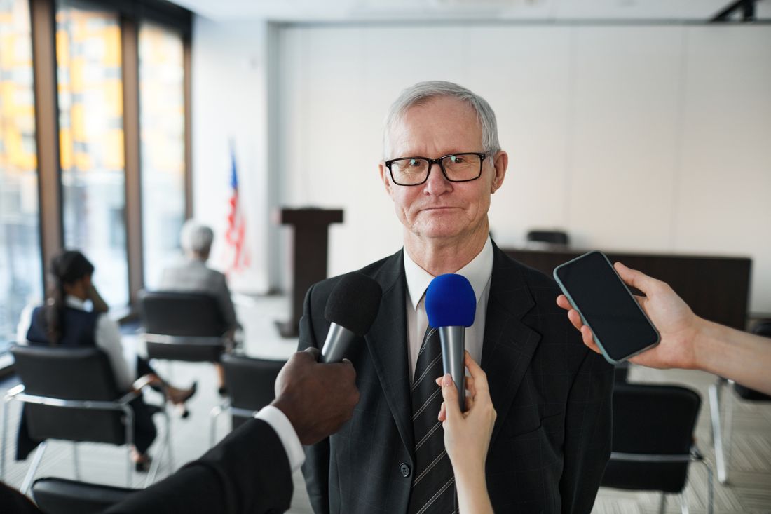 A senior businessman in formal attire being interviewed in a conference room setting.