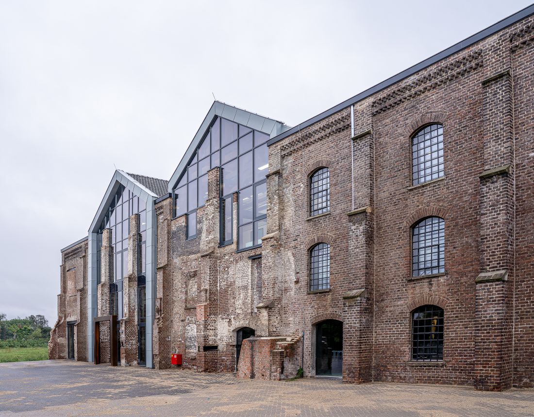 A converted brick industrial building with a contemporary glass entrance addition, photographed from across the street under an overcast sky.