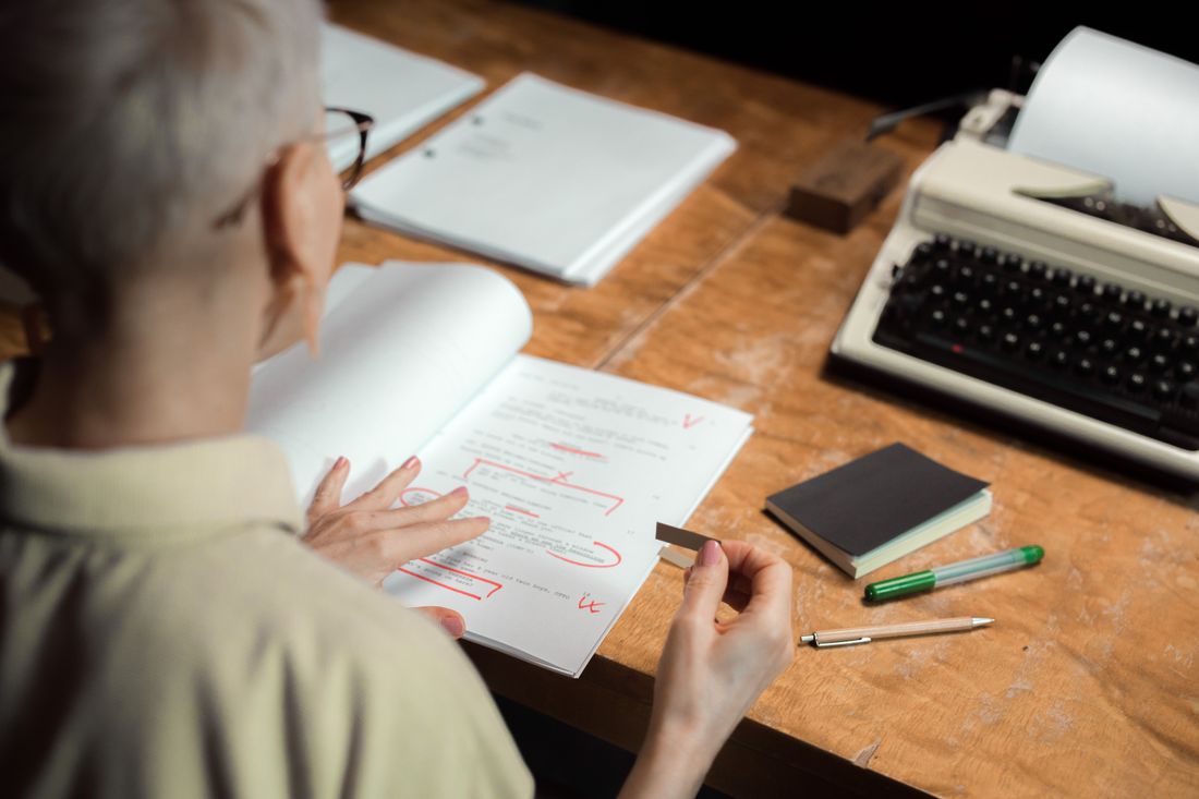 Close-up of a hand marking up a printed page with red pen corrections at a wooden desk.