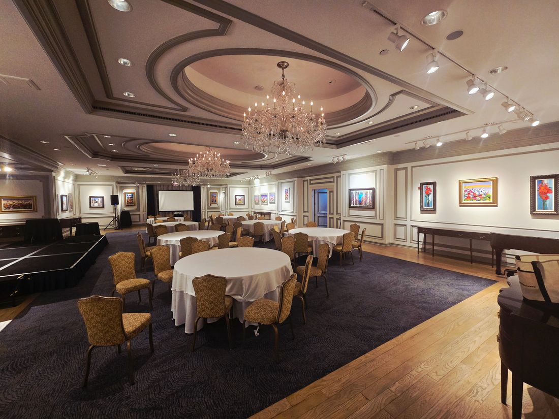 Elegant formal ballroom with crystal chandeliers, round tables set with white linens, and framed artwork on the walls