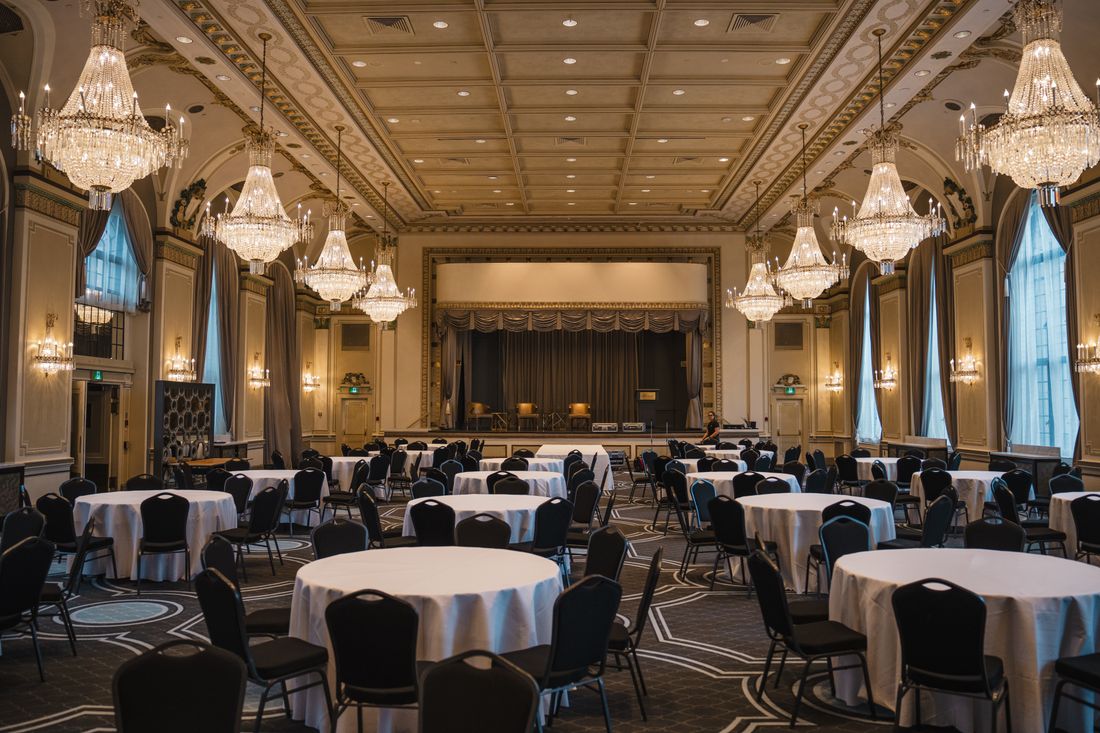 Grand ballroom set for a formal gala with round tables, white linens, and crystal chandeliers before guests arrive