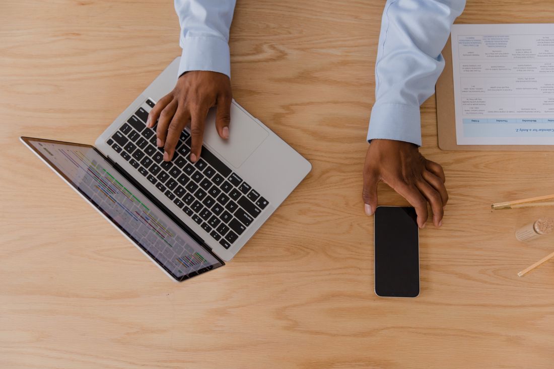 Overhead view of hands typing on a laptop at a light wooden desk with a phone beside it