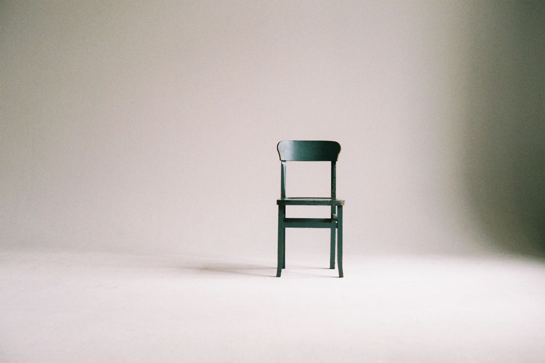 A single empty chair on a plain seamless backdrop in a quiet portrait studio