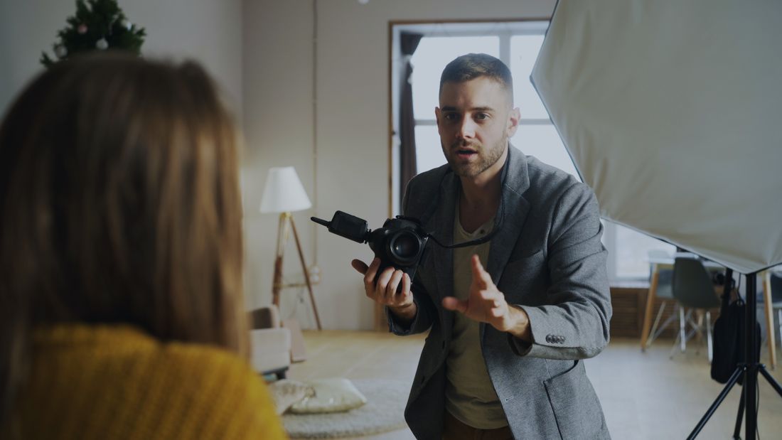 A photographer directing a subject in front of studio lighting and a softbox reflector, mid-portrait session.