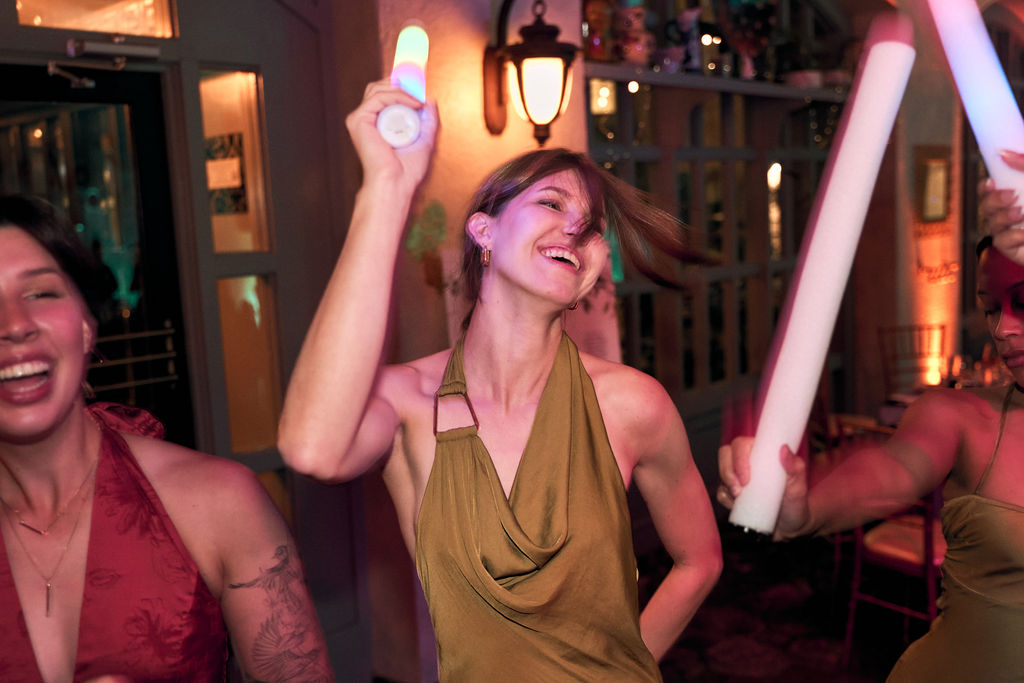Woman in gold dress dancing with glow stick at night reception.