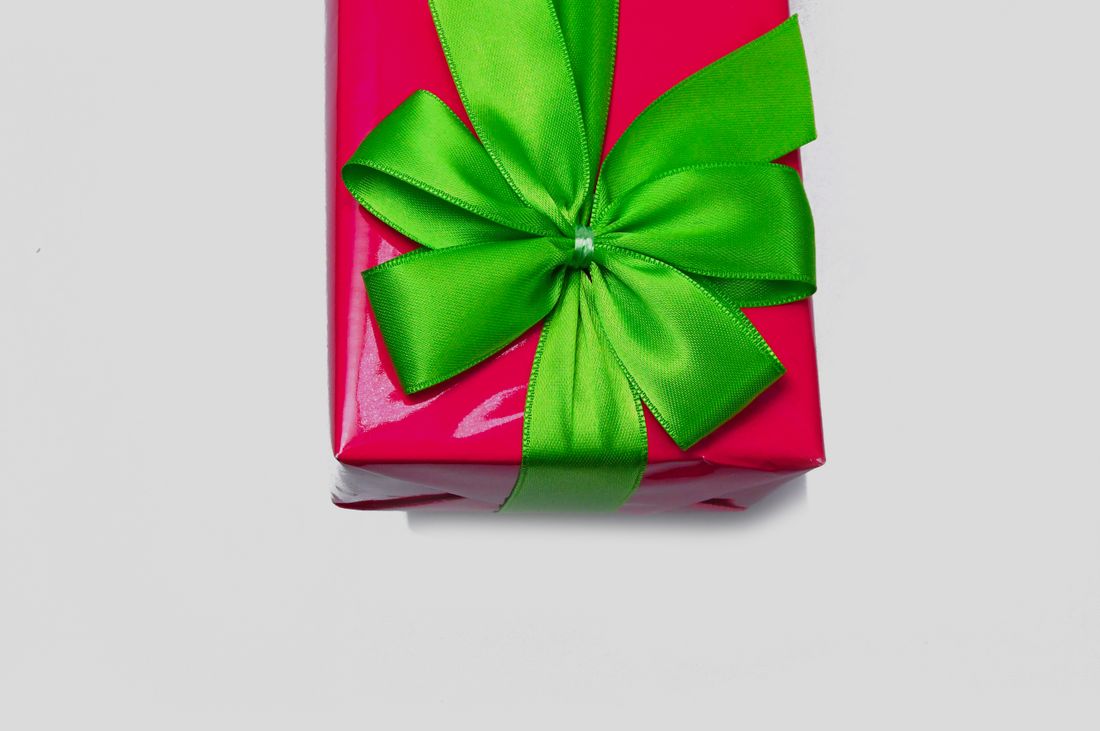 A single wrapped gift box in glossy red paper with a large green ribbon bow, on a plain light background.