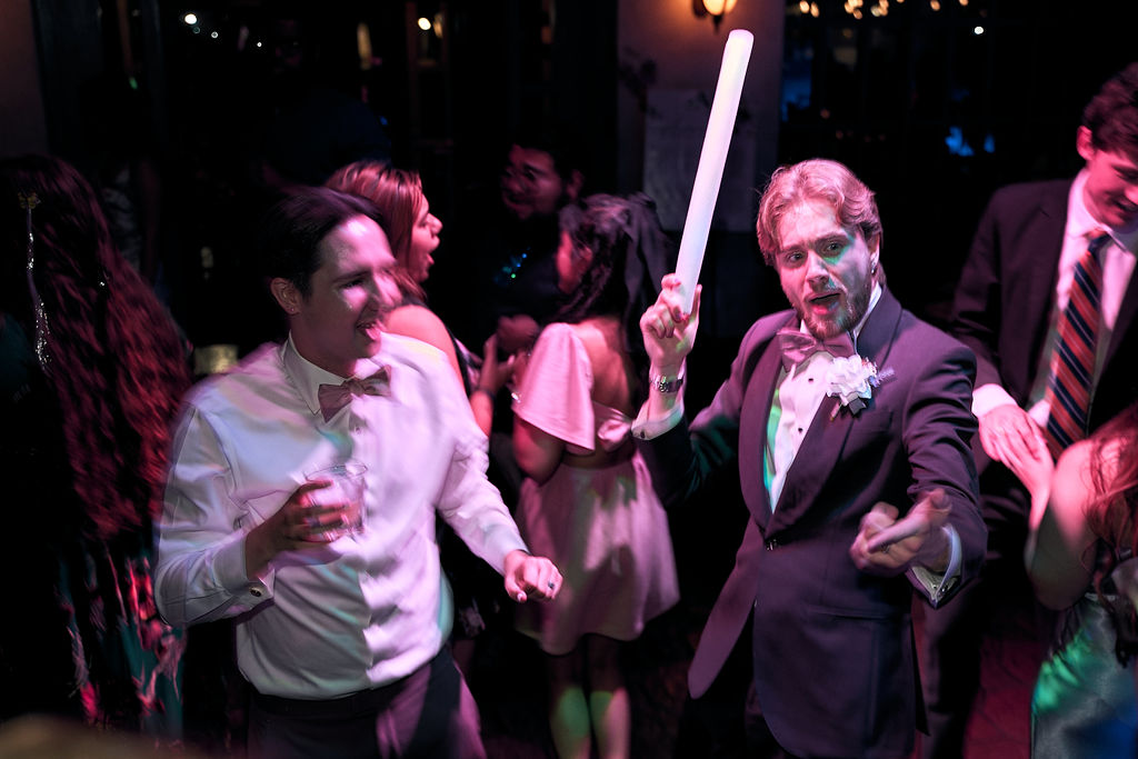 Guests in formal wear dancing under purple party lights.