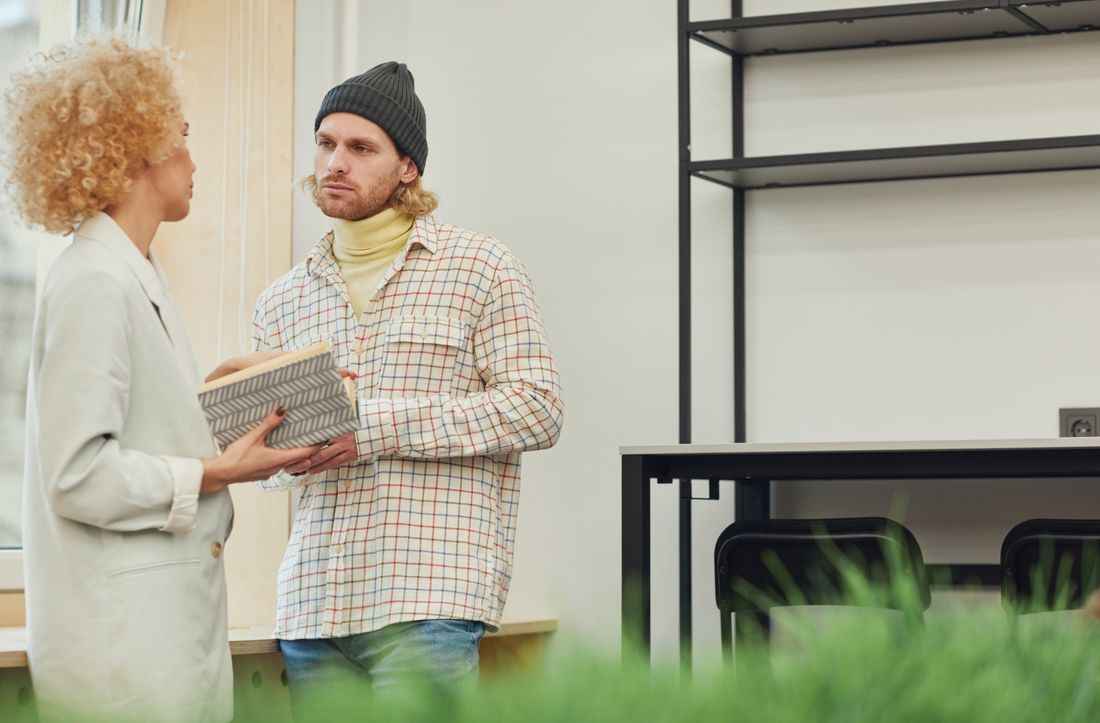 Two adults engaging in conversation holding a book in a modern office space, promoting teamwork and collaboration.