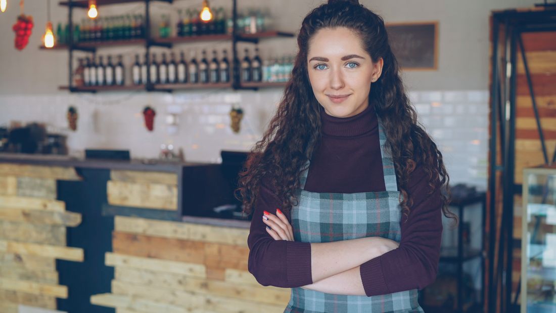 A confident restaurant owner standing with arms crossed in the space they built, environmental portrait style.