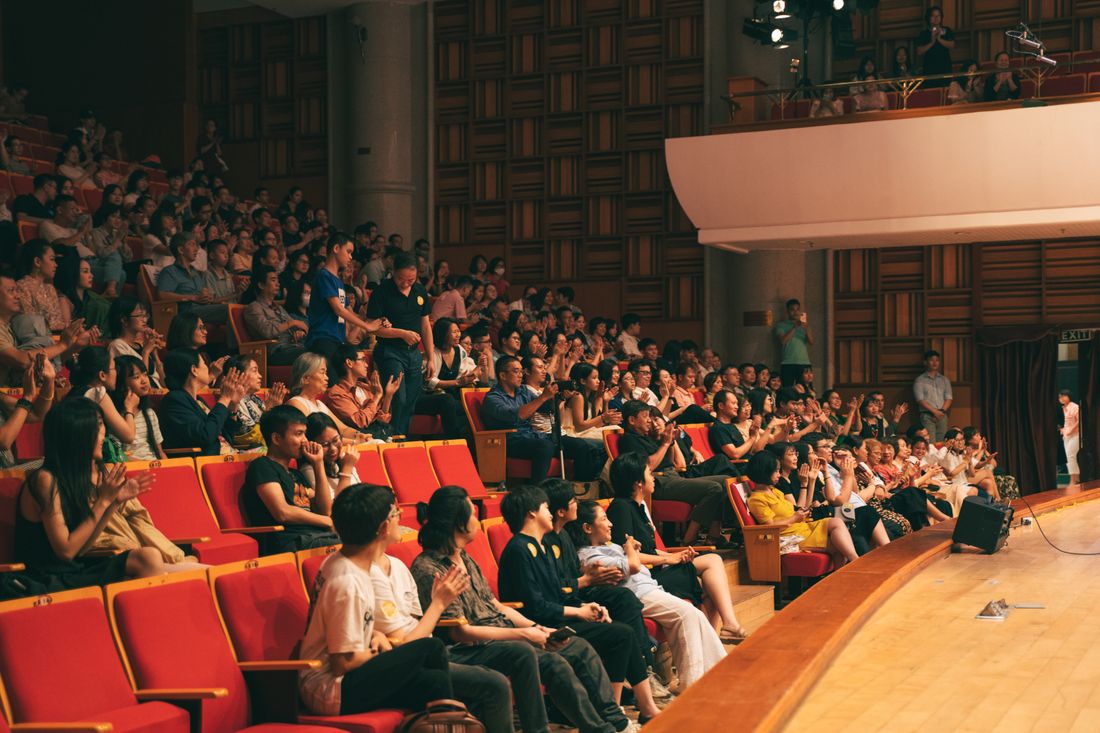A large audience seated in rows facing a lit stage in a conference hall.