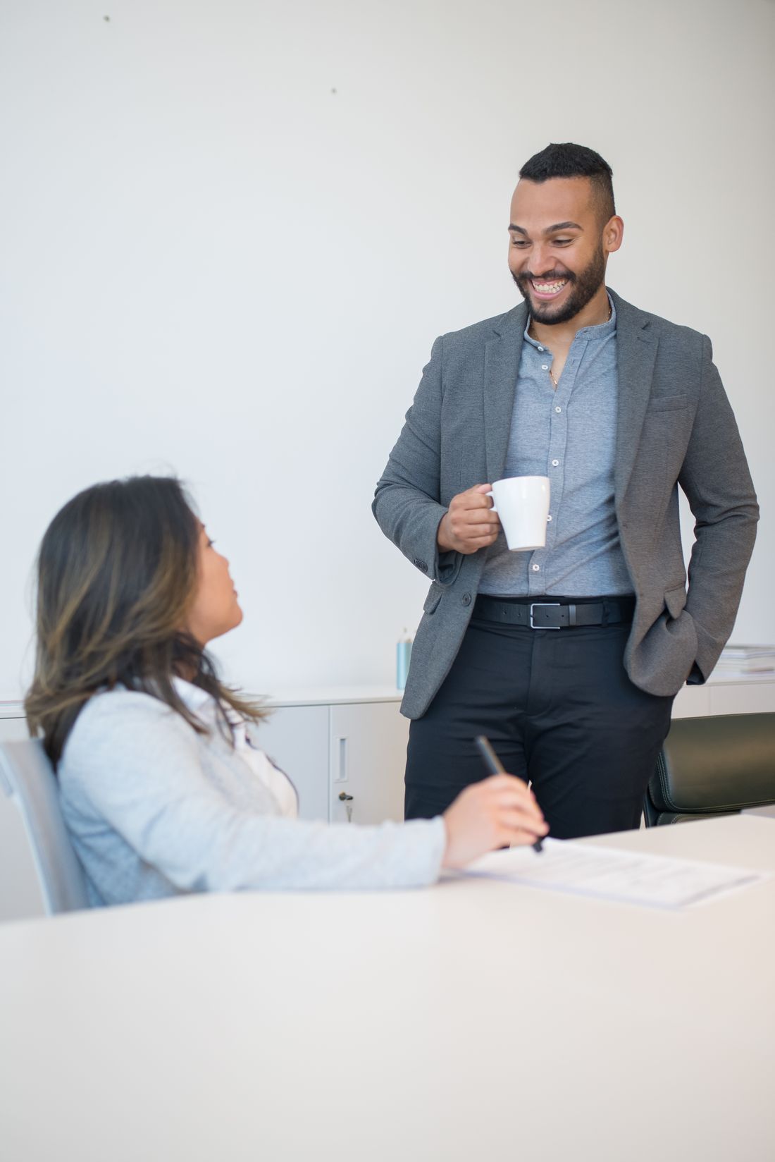 Two colleagues talking during a coffee break in a bright office setting.