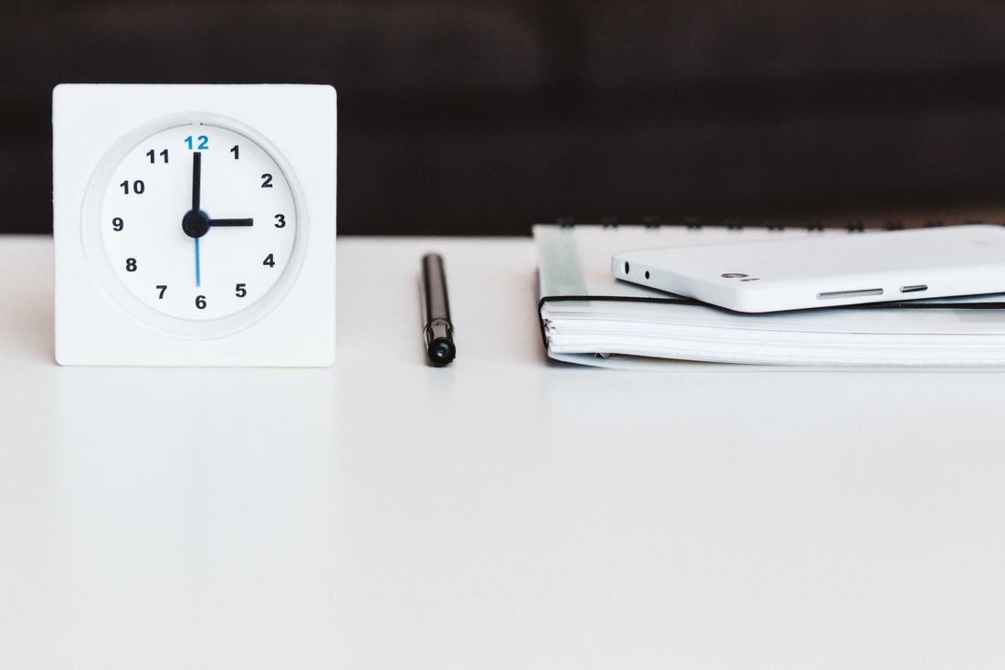 Minimalist office desk with a clock, pen, smartphone, and notebook