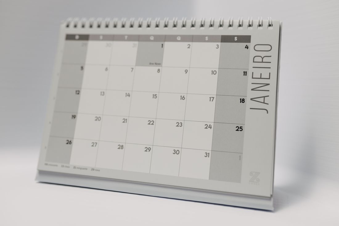 A spiral desk calendar open to a monthly grid, sitting on a table.