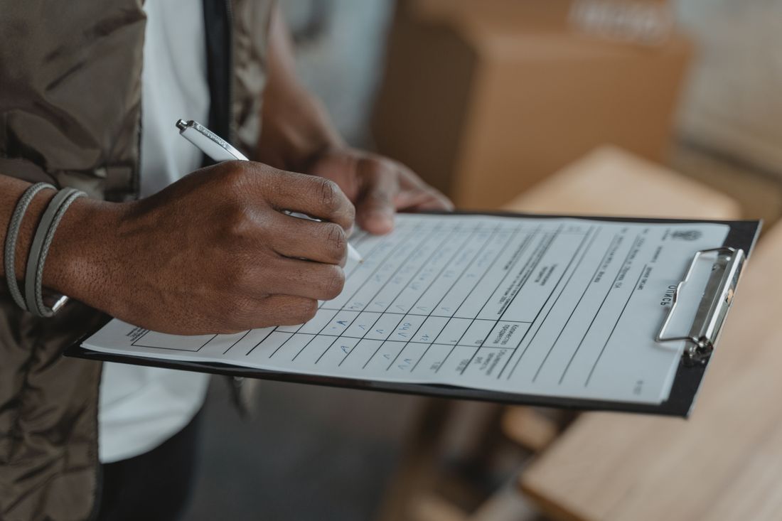 A close-up of a hand filling out a checklist on a clipboard with a pen.