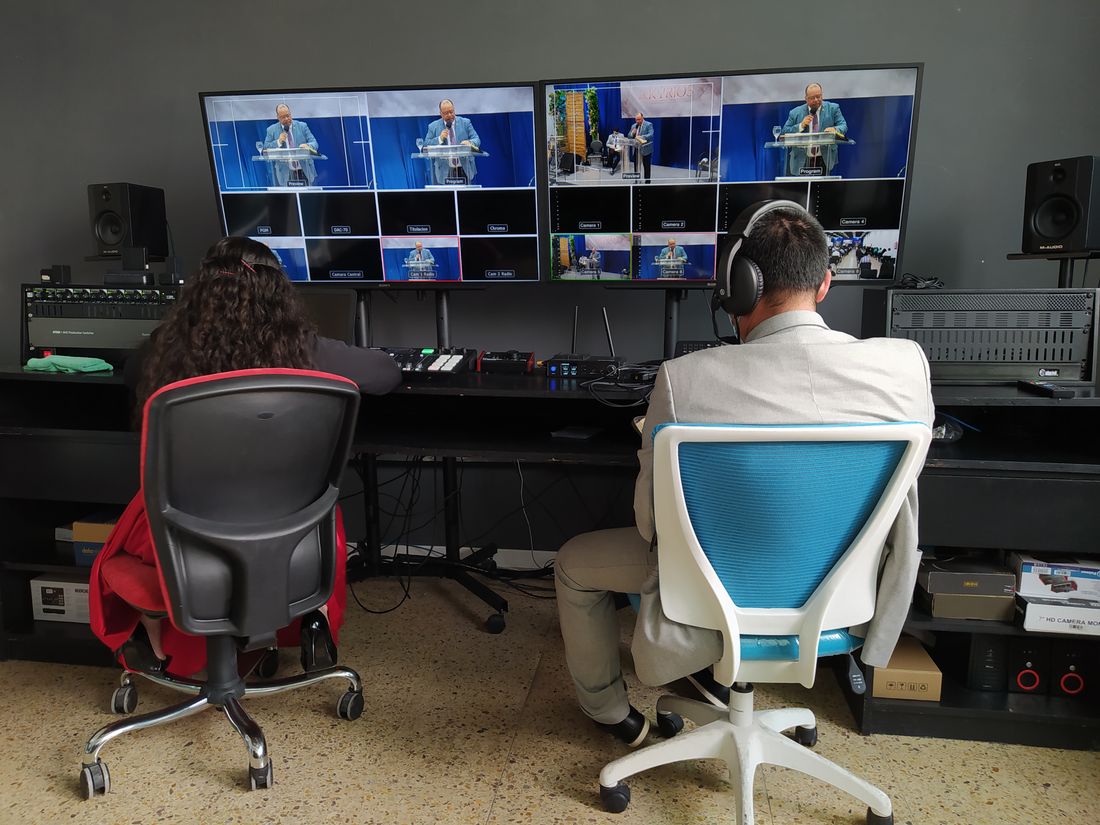 Two broadcast operators seated at a control panel, monitoring multiple live video feed screens during an event.