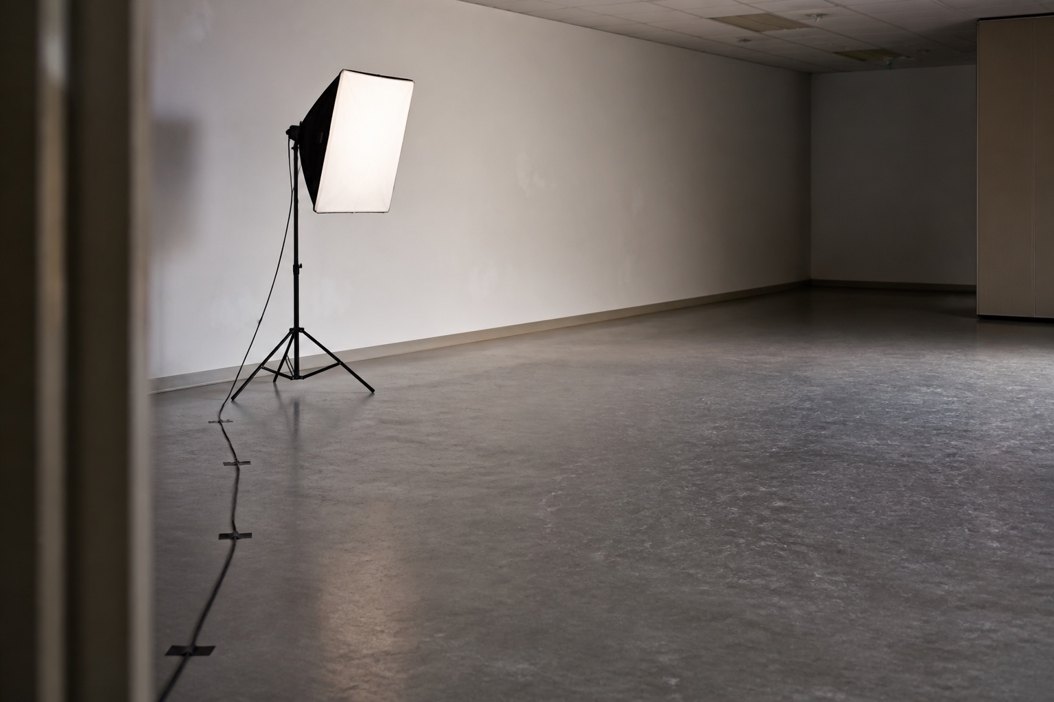 Production lighting stand with softbox and taped cable in empty event room setup.