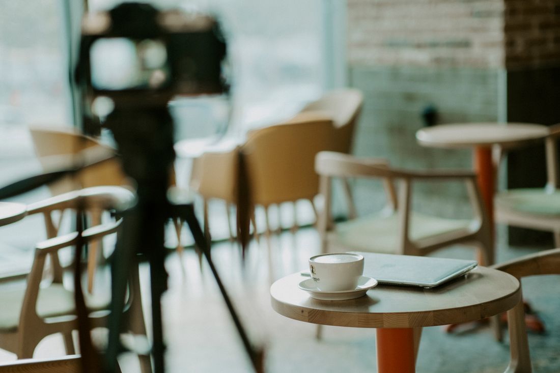 A camera on a tripod set up at a distance in an empty room with tables and chairs