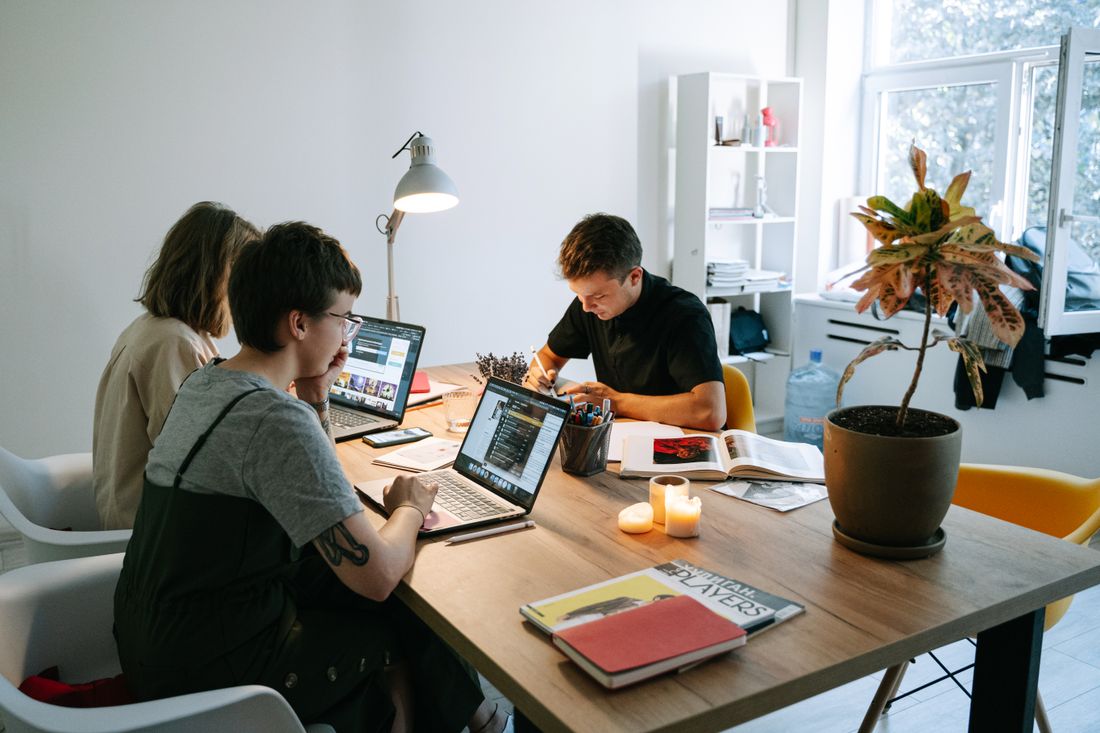 A small marketing team working with laptops around a shared table in a bright office