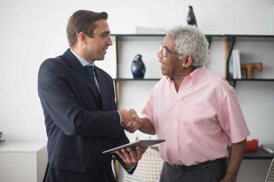 Two professionals shaking hands across a desk during an office meeting, representing the kind of trust a client places in an insurance relationship.