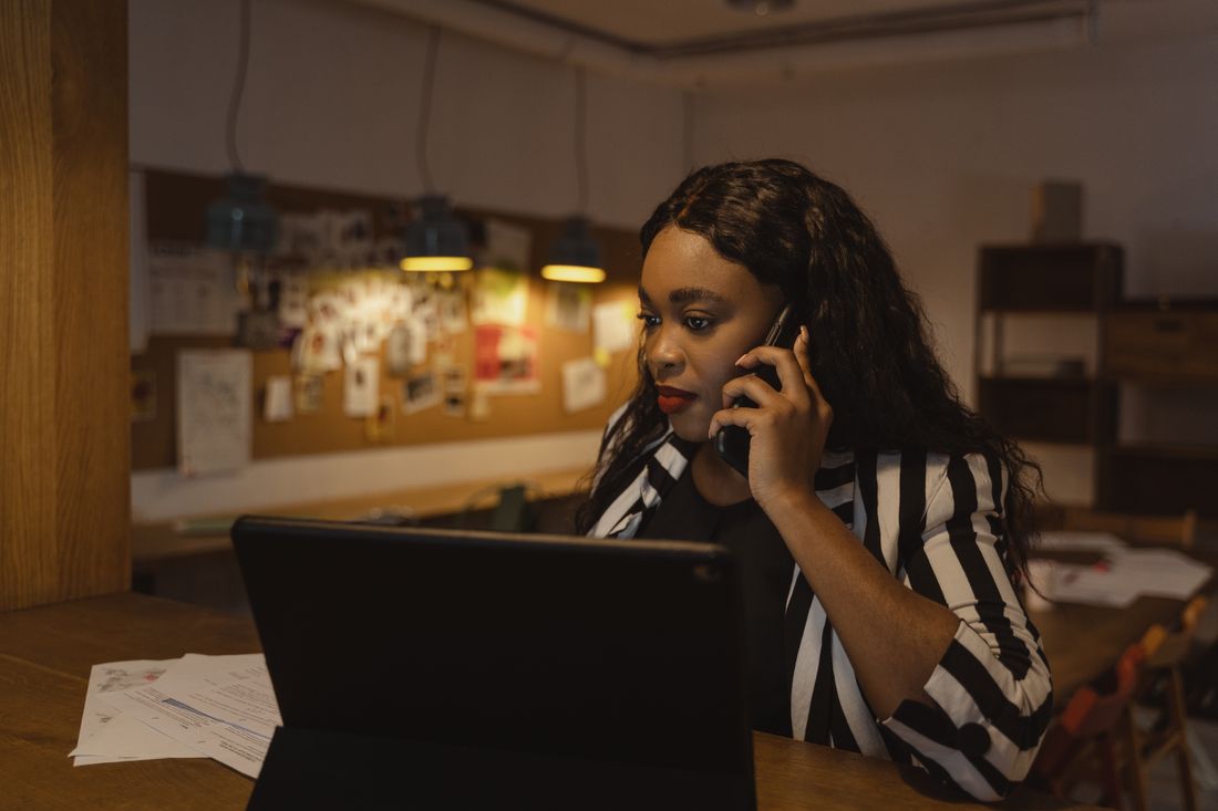 A professional in a blazer taking a phone call at her desk in a modern office.