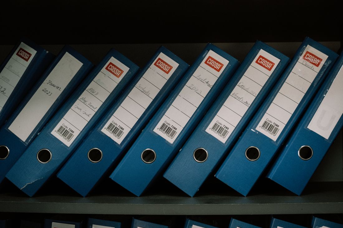 Organized binders labeled by date and name on an office shelf, representing a structured archive.