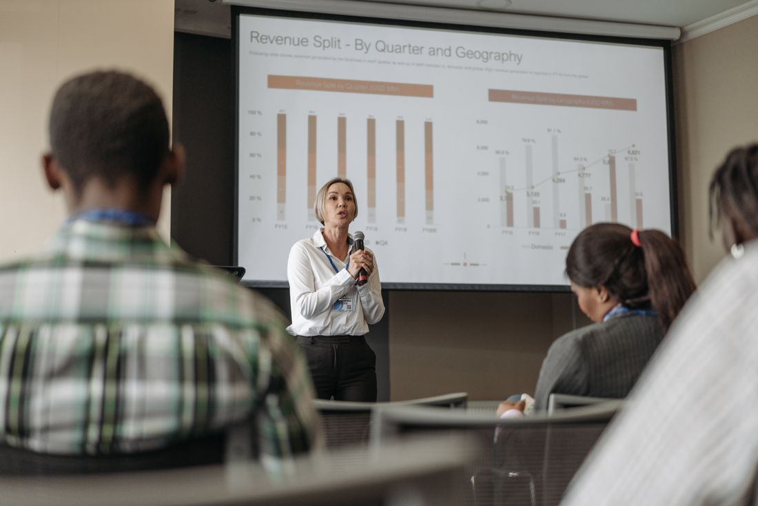 Presenter showing revenue charts by quarter and geography on a projector screen during a business conference