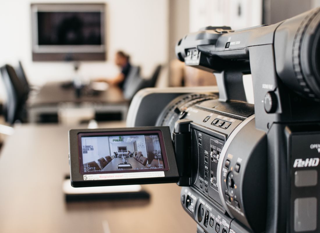 A video camera's monitor displays a shot of an empty, modern conference room set up for a video shoot.