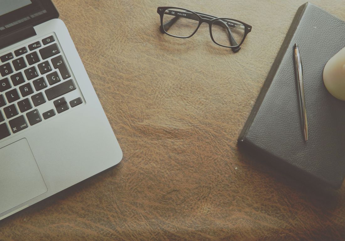 Laptop, glasses, and a closed notebook on a desk, representing discreet client materials kept out of event photography