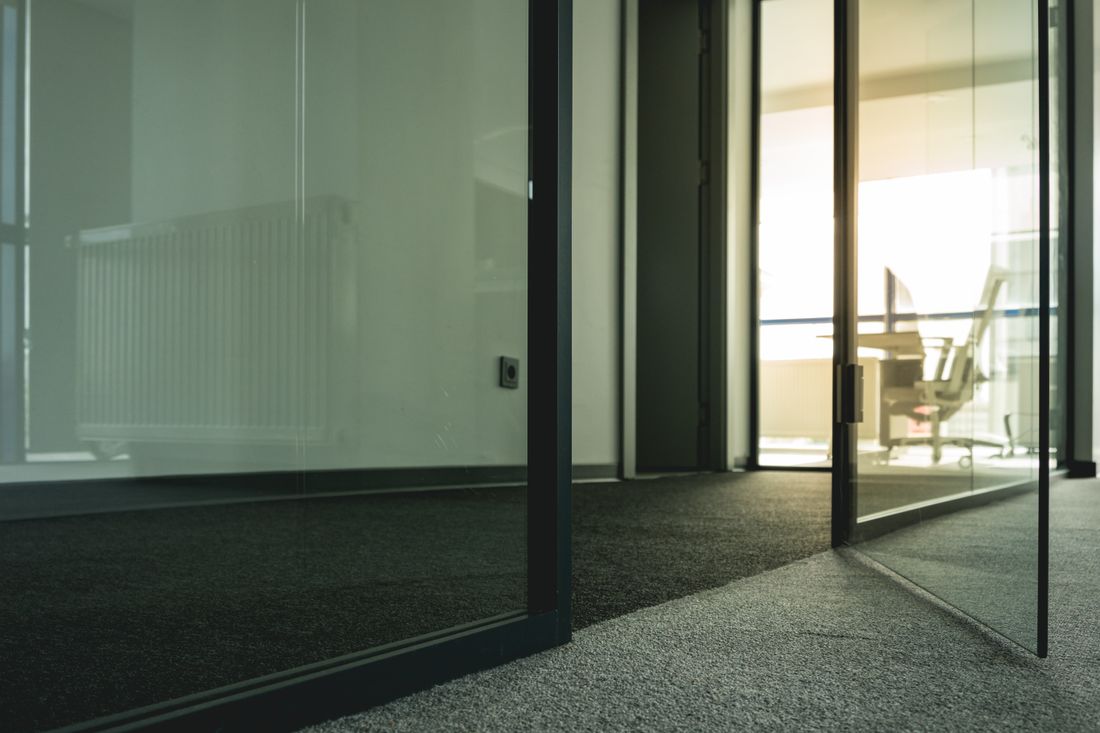 Glass-walled office corridor at golden hour with a blurred figure visible through a private meeting room door