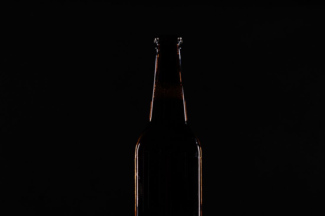 Silhouette of a single bottle backlit against a pure black background, its glass edge glowing with warm rim light and the neck and shoulder visible in dark three-quarter profile