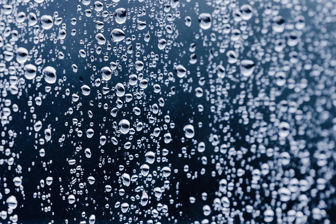 Extreme macro close-up of condensation droplets beading on cold dark glass, shallow depth of field, cool blue-toned lighting with no surrounding context