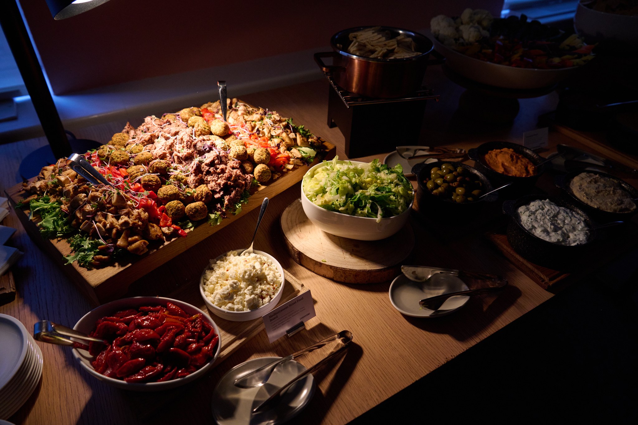 Overhead view of Mediterranean catering spread with falafel, vegetables, and dips on wooden table.