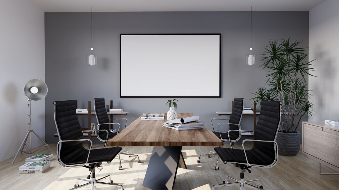 A small meeting room with a blank presentation screen and chairs arranged loosely around a wooden table.