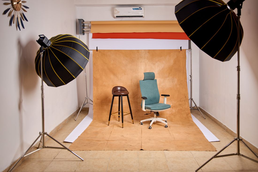An empty photography studio set up with backdrop paper, an office chair, and studio lighting, ready for a headshot session.