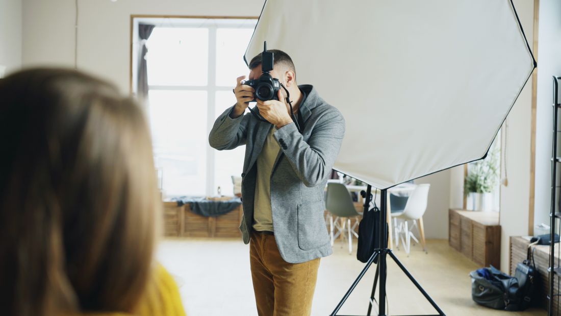 A photographer captures a portrait using a large softbox in a bright studio, the subject seen from behind.