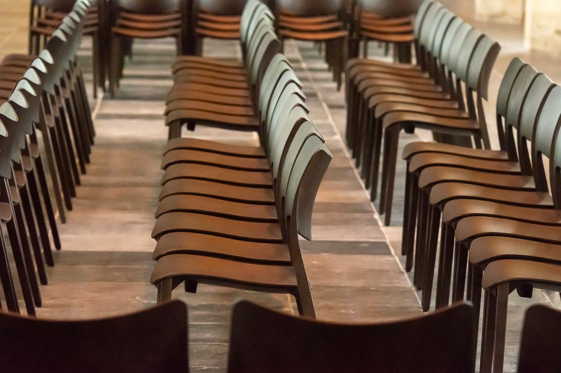 A close view of empty wooden chairs set in straight rows on a stone floor, with a narrow aisle between them.