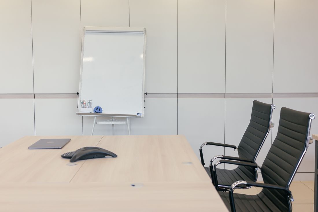 An empty modern conference room with a blank whiteboard, chairs, and a table, ready for a meeting.