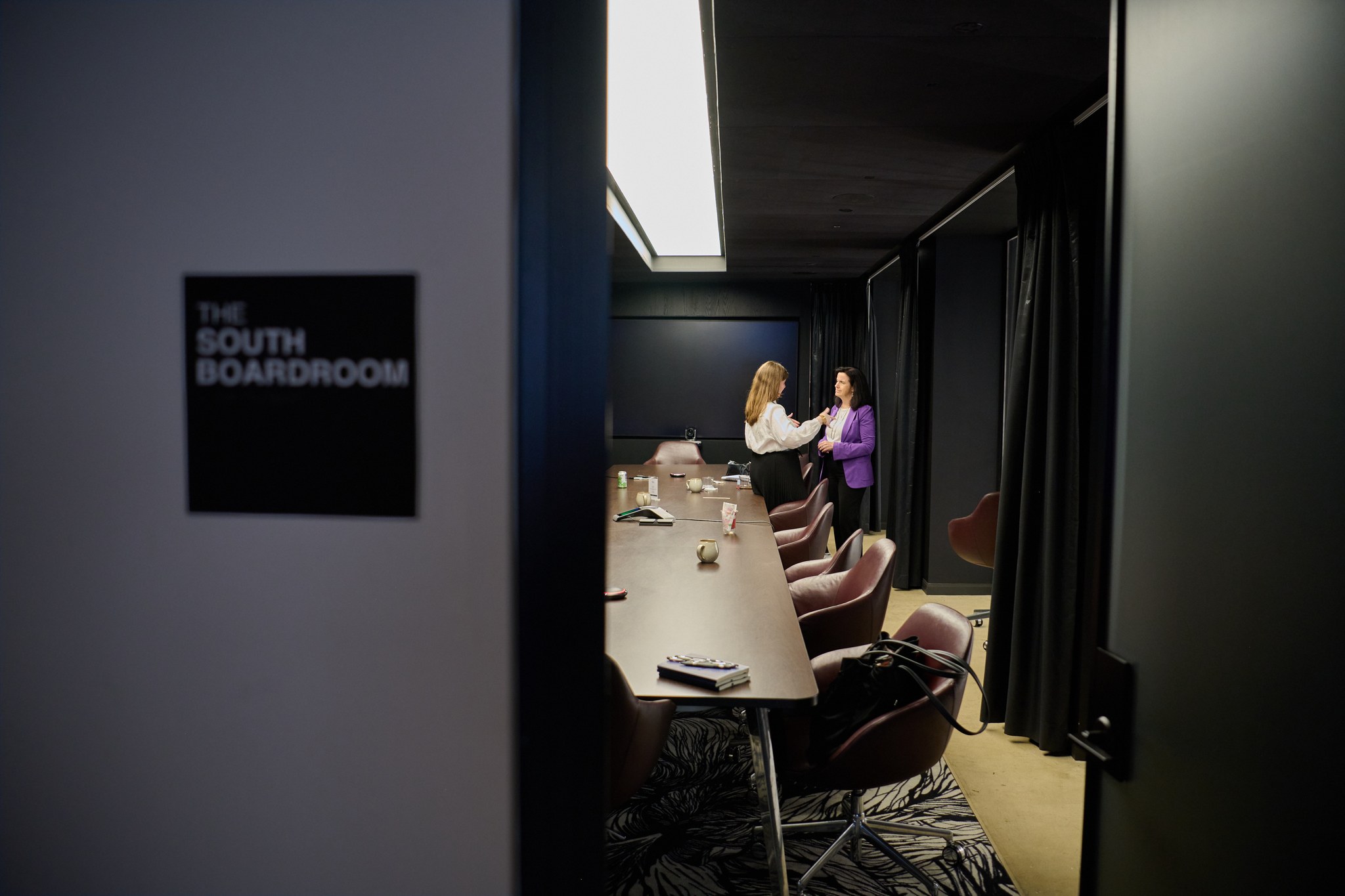 Two professionals have a conversation in a private boardroom meeting space.