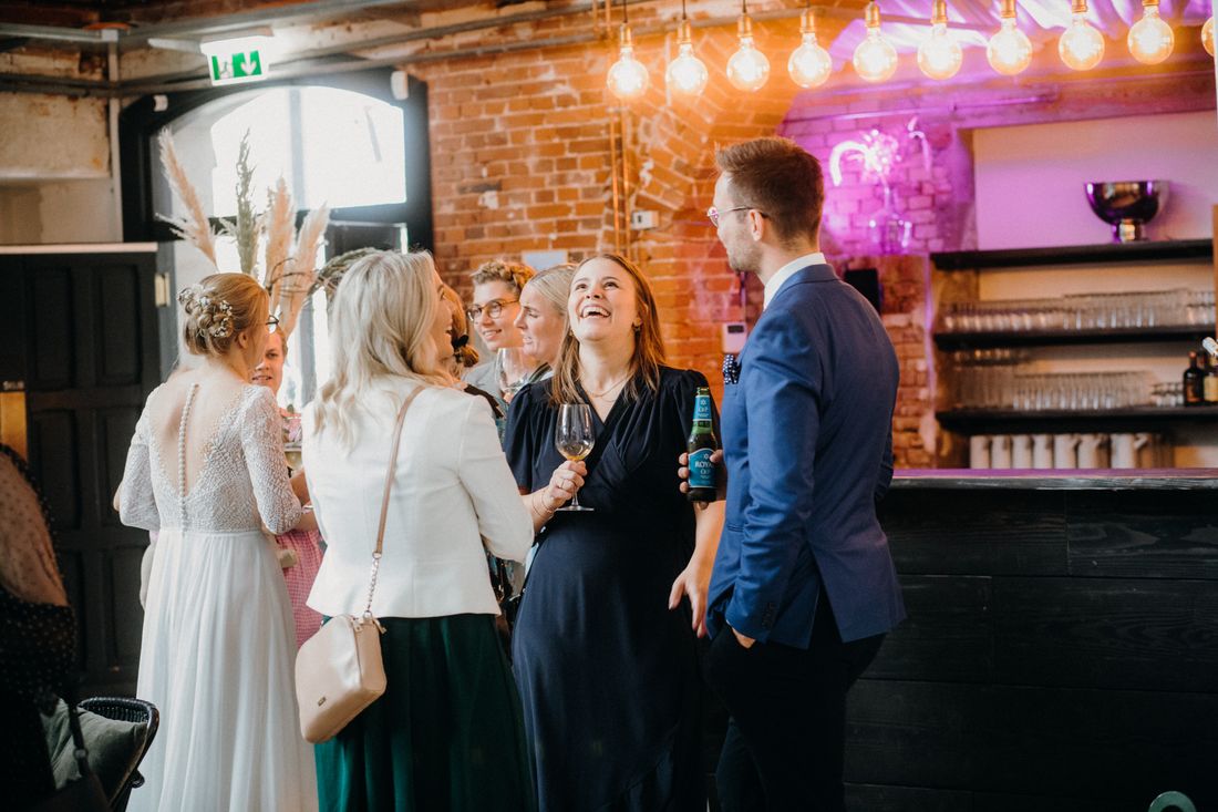 A small group of guests stand close together, mid-conversation and smiling, at an evening networking gathering.