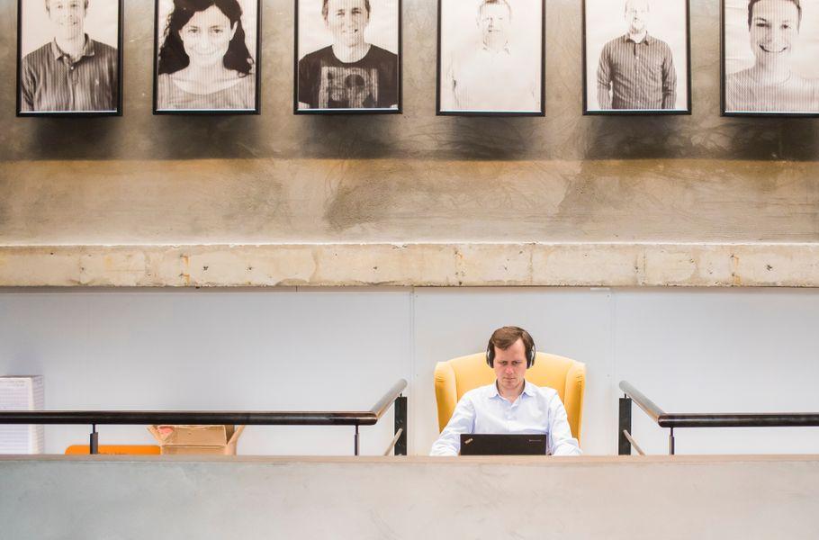 A row of framed black-and-white staff portraits hangs above a concrete ledge, with one person working at a desk below.