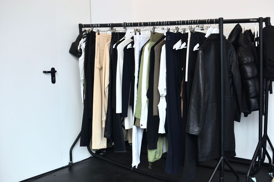 A rolling wardrobe rack with several outfit changes hung ready in a plain studio room