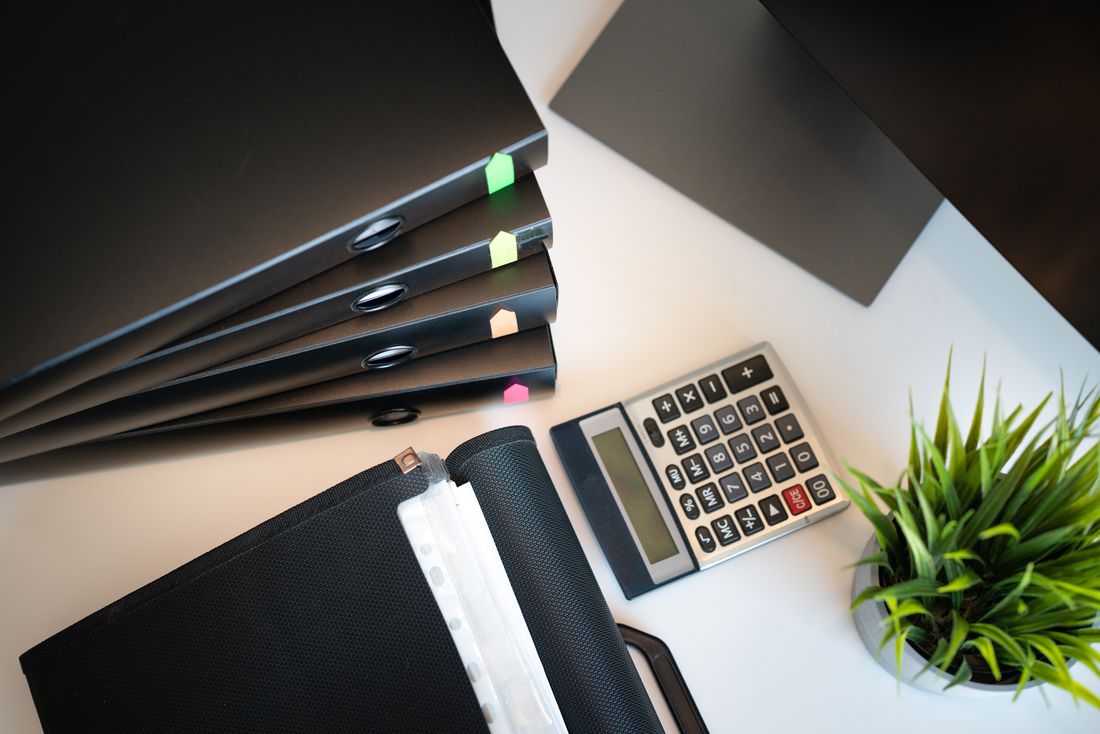 A tidy desk with binders, a calculator, and a small plant, set up for handling paperwork.