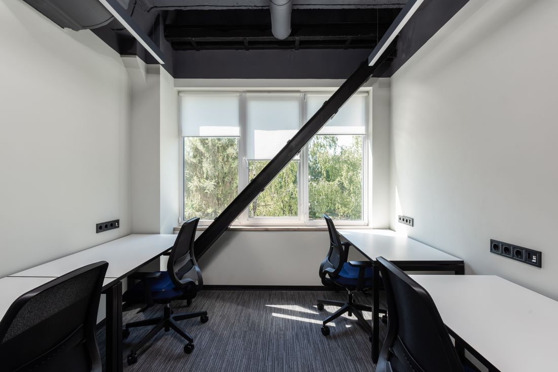 A newly finished, empty office space with bare white desks and chairs, daylight streaming through a large window before anyone arrives.