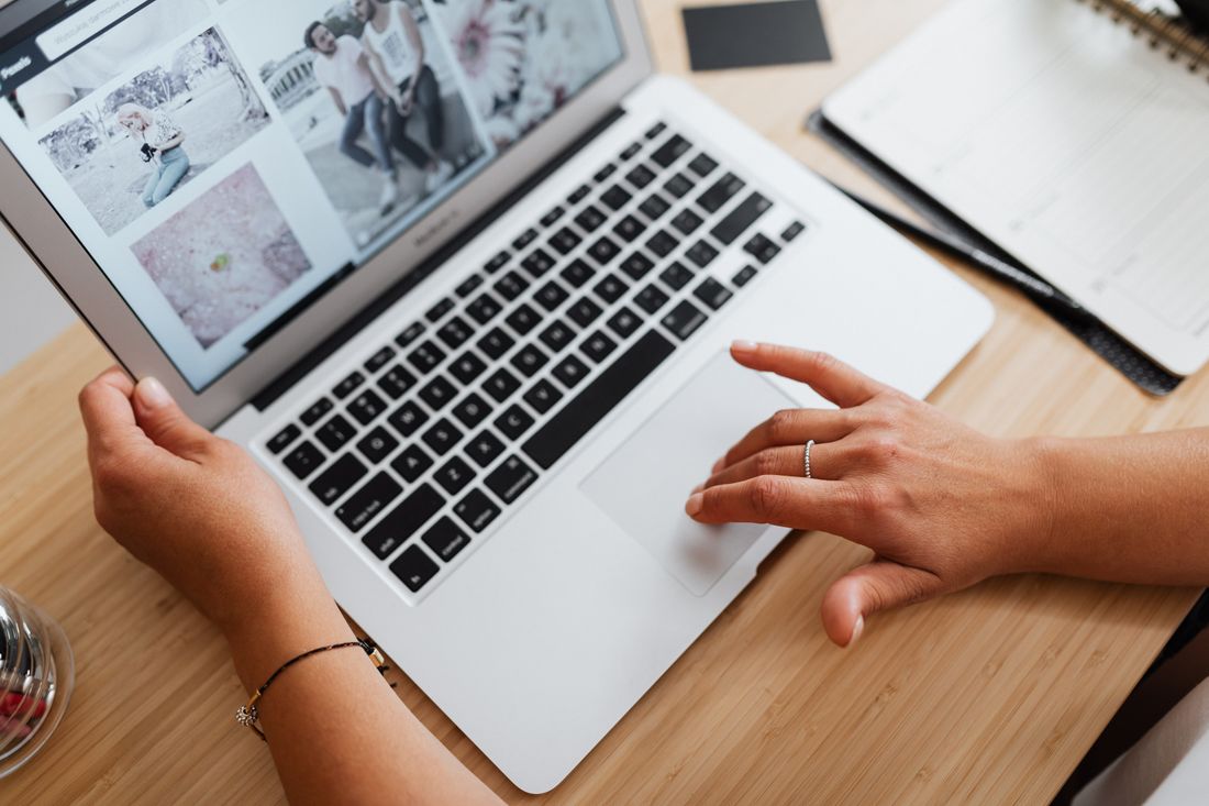 Close-up of hands scrolling through a photo gallery on a laptop at a desk