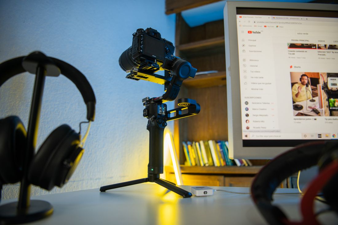 Camera on a gimbal stabilizer set up beside a monitor showing a video content dashboard, representing an ongoing content library workflow