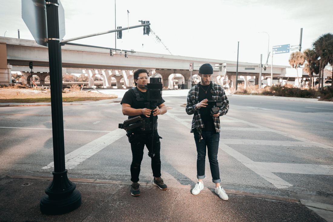 Two crew members with camera equipment standing together on a city street, representing a coordinated two-person shoot