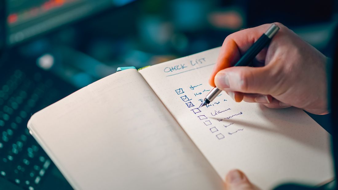 A hand checking off items on a handwritten checklist, representing a shot list used to coordinate a shoot
