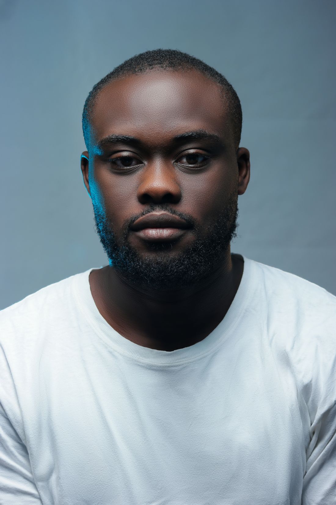 A clean, neutral studio portrait of a man in a plain white shirt against a plain gray background, the kind of consistent current portrait a bio update can keep using.