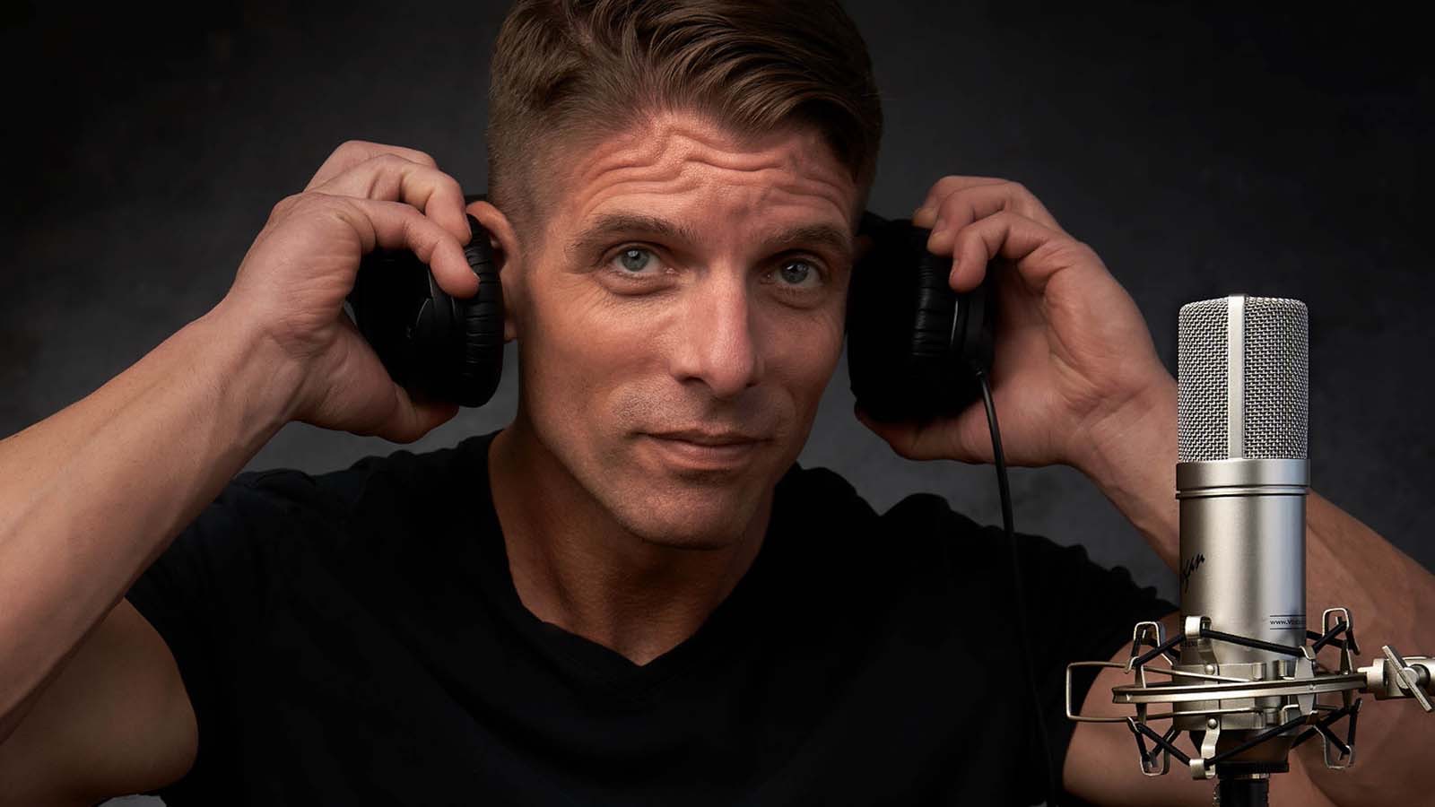 Close-up of a man adjusting his headphones beside a studio microphone