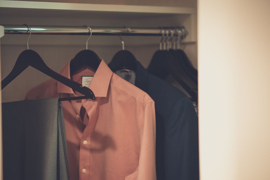 A formal suit and dress shirt hanging neatly among other clothing in a wardrobe